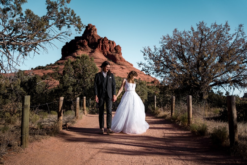 Wedding Photographer, a husband and wife walk hand in hand down a desert path in their wedding attire